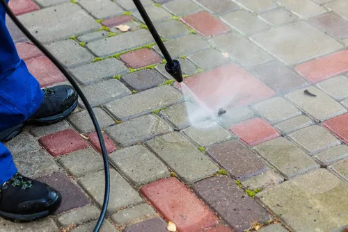 A technician cleaning moss and grime from red and gray pavers with a pressure wand